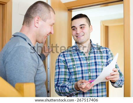 Smiling lodger talking neighbor with papers at doorway. Focus on the right man