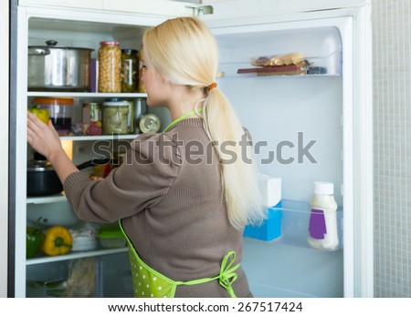 Blonde american woman looking for something in fridge at home kitchen