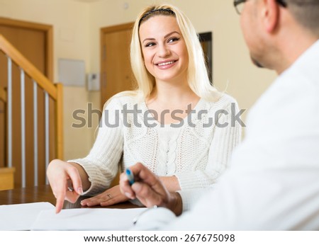 Couple filling in documents at home. Happy smiling woman points with her finger where to sign
