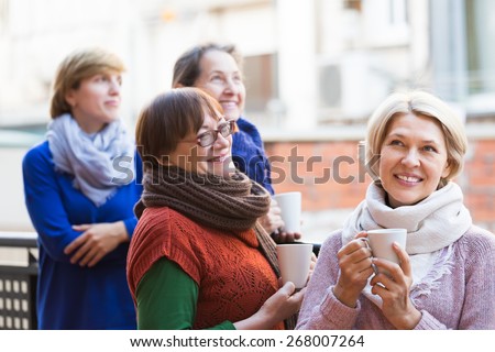 Positive smiling elderly women drinking coffee at patio. Focus on blonde