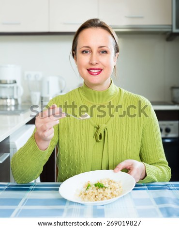 Cheerful woman sittin at the table in kitchen eating rice