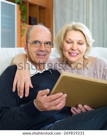 Portrait of smiling senior mature spouses with picture album indoors. Focus on man
