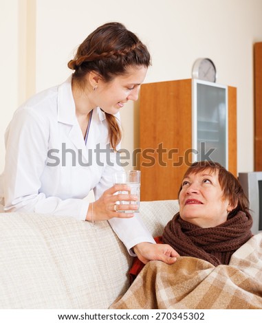 caring nurse giving glass of water to  mature woman at home