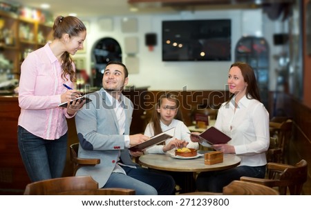 Beautiful waitress and smiling family with child reading menu. Focus on the waitress