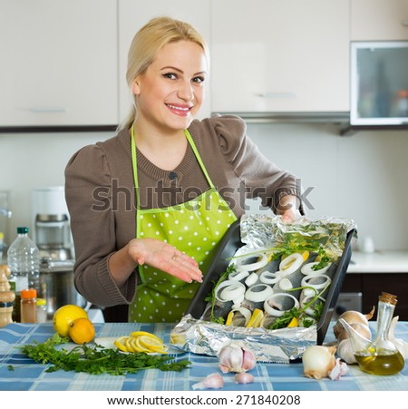 Smiling girl with raw fish on roasting pan at home kitchen
