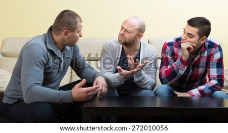 Three male friends sitting at the table at home and sharing the problems