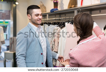 Happy young girl with boyfriend choosing new apparel in clothing store