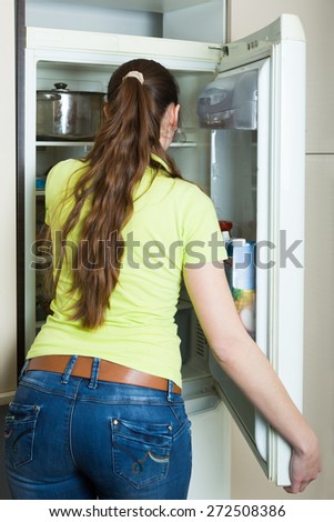 Young woman carefully inspecting refrigerator shelves indoors