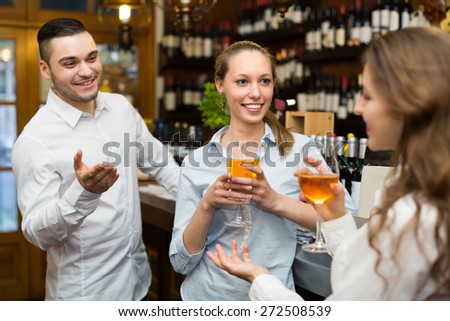 Two positive smiling girls with man chatting at bar of restaurant. Focus on girl
