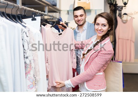 Handsome husband helping happy wife to choose new clothes in market