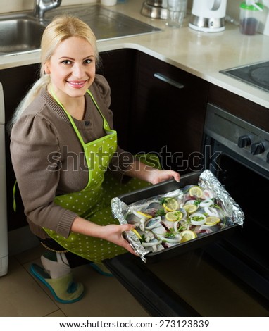 Smiling woman cooking fish  in oven at home kitchen