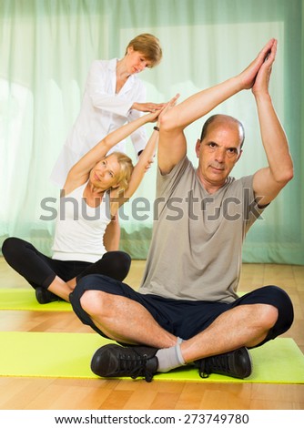 Medical staff helping senior couple to take correct position at gym