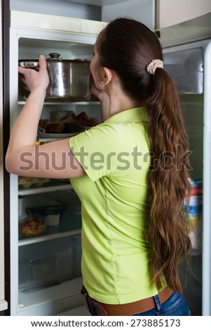 Young brunette woman carefully inspecting refrigerator shelves indoors