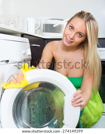 Smiling young blonde woman cleaning washing machine at home kitchen