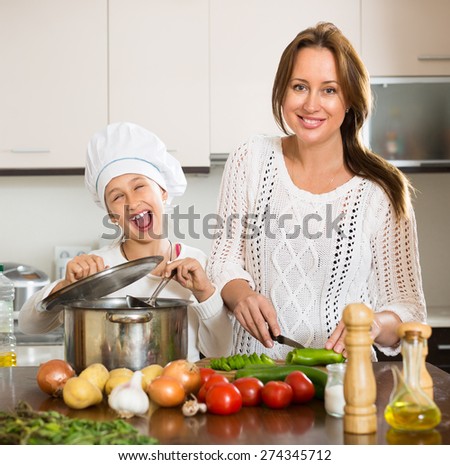 Portrait of playful daughter and mom with vegetables and casserole at domestic kitchen