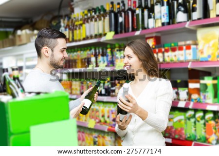 Adult positive european shoppers choosing bottle of wine at liquor store