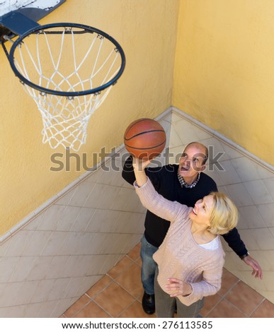 Positive smiling senior family couple playing basketball in patio. Focus on woman