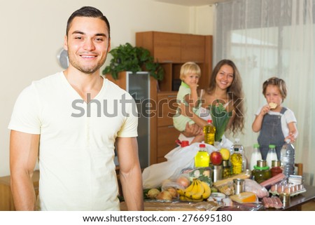 Young family with little children sorting purchased food out at home. Focus on man