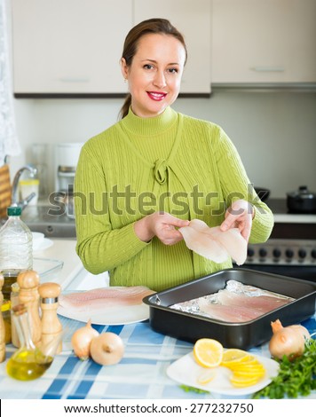 Smiling woman cooking filleted fish at home kitchen