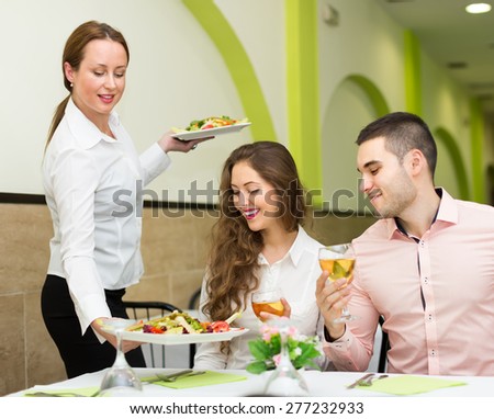 Female waiter with plates in hands serving guests table in restaurant. Focus on girl