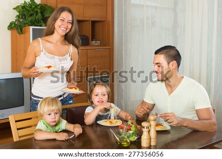Happy family of four having lunch with spaghetti at home