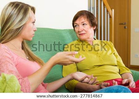 Mother and adult daughter sitting on sofa and having serious conversation