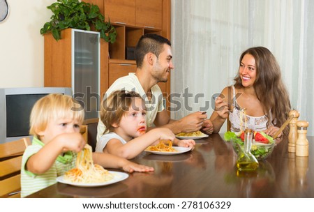 Happy young family of four eating with spaghetti at table