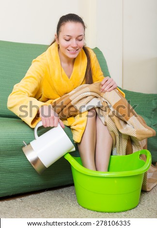 Smiling woman warming feet in basin with hot water indoors
