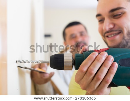 Two positive skilled men with drill and level at home. Focus on drill