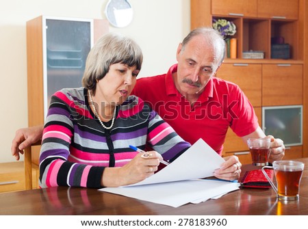 serious mature couple reading financial document together at home