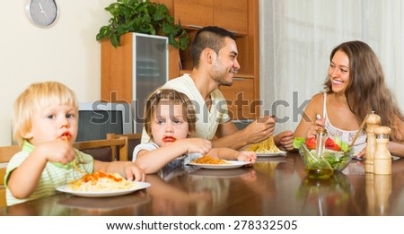 Smiling parents with children having lunch with spaghetti at home together. Focus on man