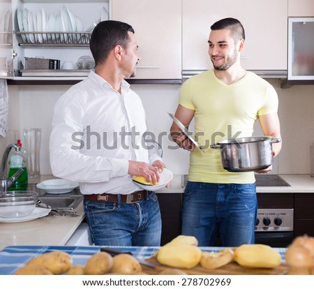 Two cheerful men cooking and doing dishes at home kitchen. Selective focus