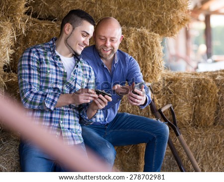 Portrait of two joyful smiling male farmers with phones at hayloft