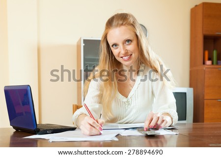 Positive blonde woman working with financial document and laptop at home