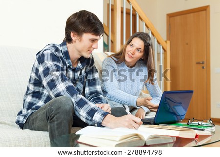 Two students guy and girl preparing for session together with electronic book and laptop in sofa