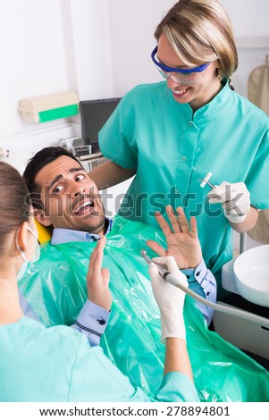 Dentist with assistant and scared male patient at surgery office
