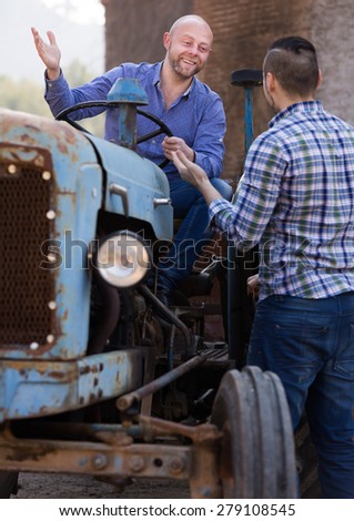 Two happy farmers talking near agricultural machinery in the shed