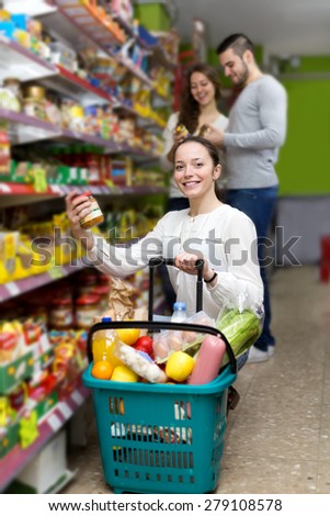 Cheerful woman standing near shelves with canned goods at shop