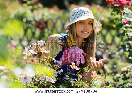 Happy young female  in uniform at yard gardening with roses