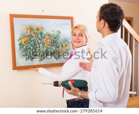 Young man and woman hanging art picture in frame