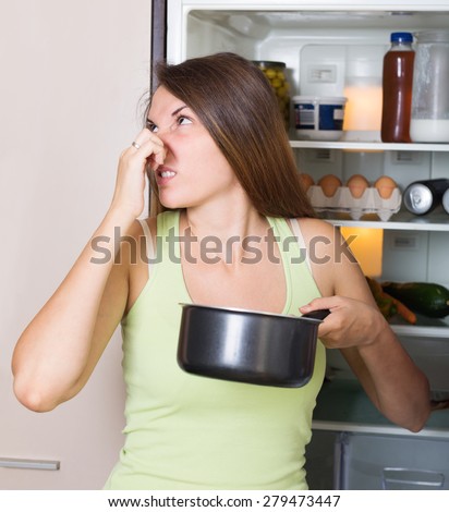 Young woman holding foul food near refrigerator in house