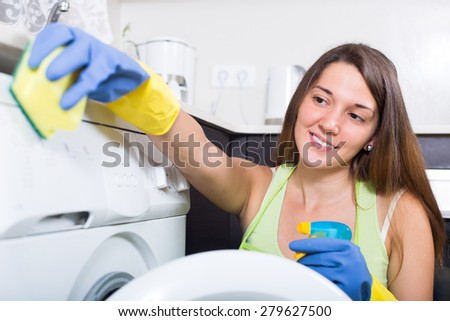 Happy young girl cleaning washing machine at home kitchen