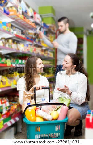 Smiling women standing near shelves with canned goods at shop