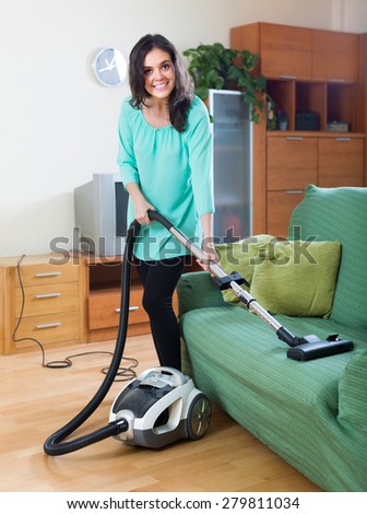 Young smiling woman cleaning with vacuum cleaner at home