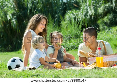 Young cheerful family with little daughters having holiday with picnic at park in summer day