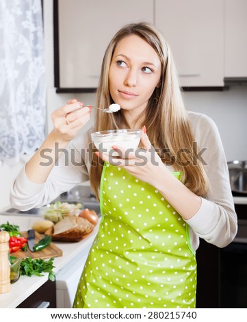 Smiling woman in apron eating curd cheese in kitchen