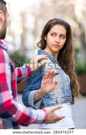 Man is trying to pick up girl on city street outdoors. She is irritated by him and refuses to talk