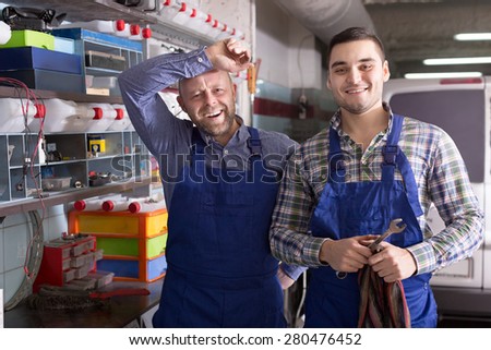 Two workmen standing near the storage shelves in auto repair shop