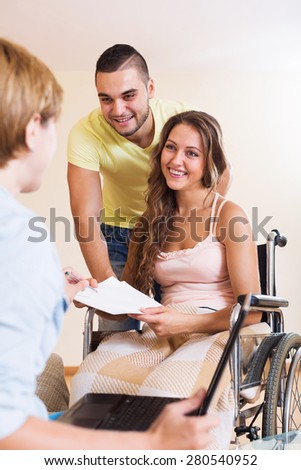 Positive man and handicapped wife on wheelchair having discussion with social worker