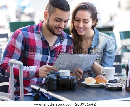 Young travelers with photocamera and map at open-air cafe. Focus on man